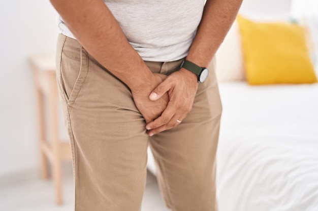 Young latin man covering his genitals with hands at bedroom