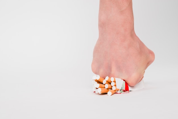 A person fist crushing packet of cigarettes over white background